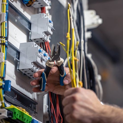 Male electrician at the checkout counter on a blurred background of a switchboard.